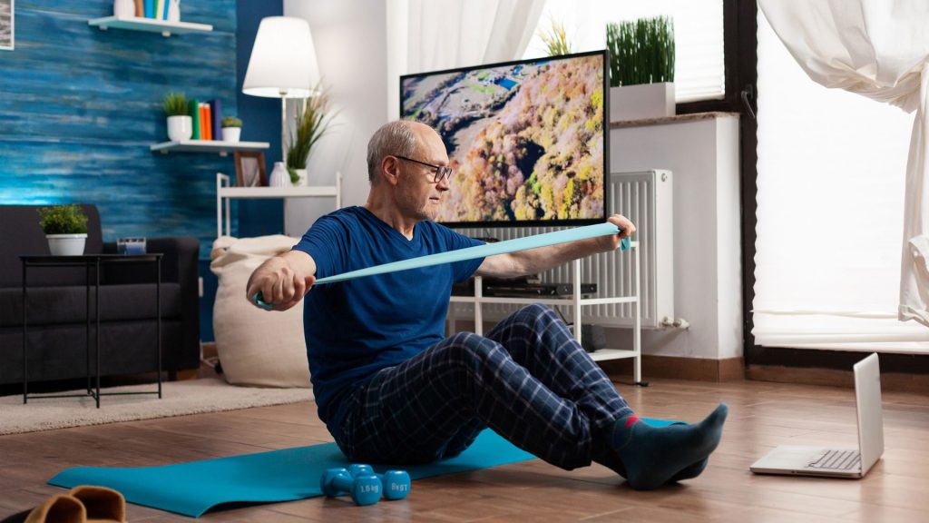 Older man exercising on a mat at home in front of a screen