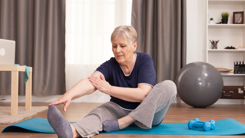 Older woman stretching on an exercise mat at home